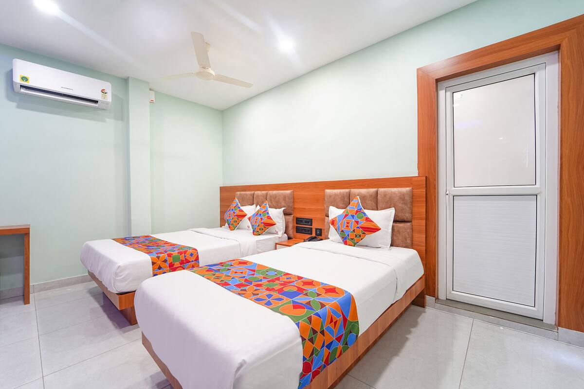 A hotel room with two beds, a ceiling fan, an air conditioning unit, and a large window with a wooden frame.