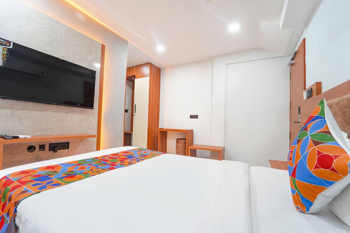 A modern hotel room with a large bed, a flat-screen TV mounted on the wall, a wooden nightstand, and a desk with a chair.