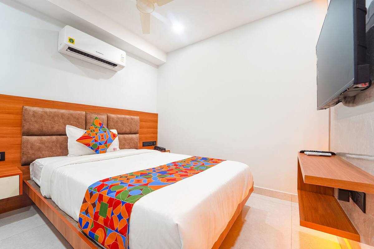 A hotel room with a bed, a TV, an air conditioner, and a wooden nightstand.