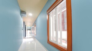 Un couloir aux murs bleu clair, avec une fenêtre à cadre en bois et un sol carrelé de carreaux blancs.