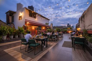 An outdoor dining area with tables and chairs, surrounded by potted plants and a building with a red-tiled roof. - Fabhotel India International (New Delhi)