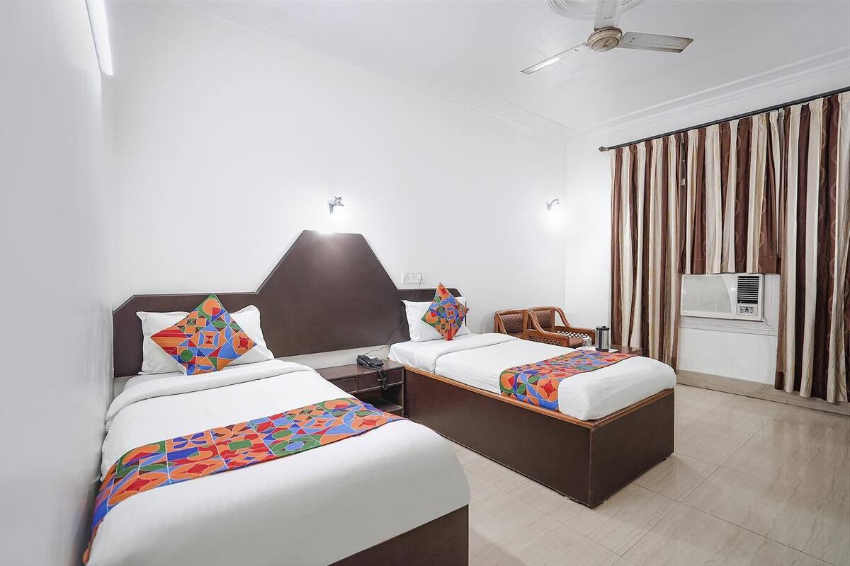 A hotel room with two beds, a ceiling fan, an air conditioning unit, and a window with curtains.