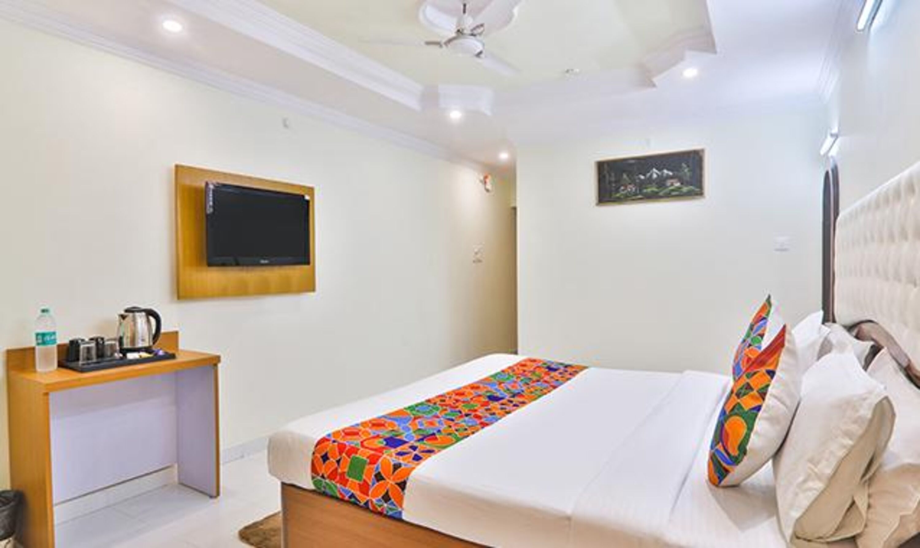 A hotel room with a bed, a desk, a television, and a ceiling fan.