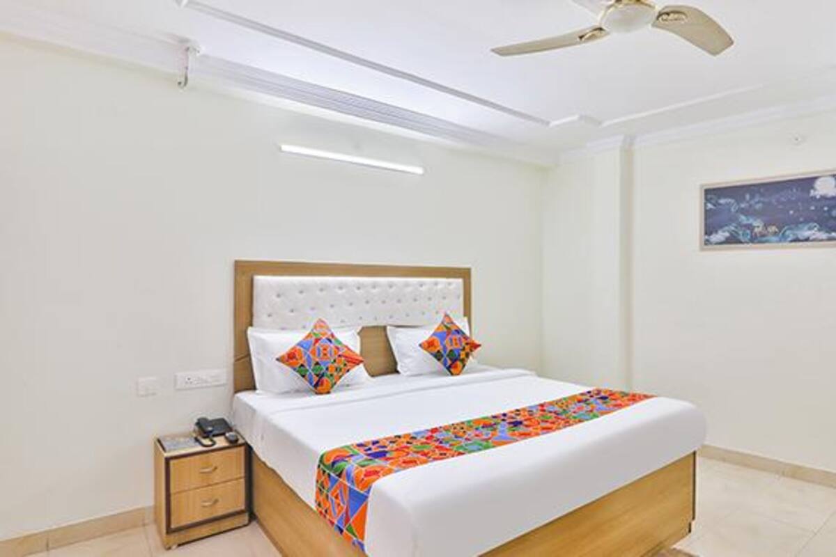 A bedroom with a bed, a nightstand, a ceiling fan, and a painting on the wall.