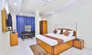 A bedroom with a large bed, a wooden wardrobe, a desk with a chair, and a television.