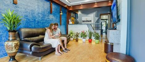Un espace d’accueil avec un mur bleu à texture, un canapé en cuir et une enseigne sur laquelle on peut lire « SWARNAM ».