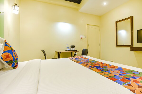 Habitación de hotel con una cama, un escritorio, una silla, una mesa con una botella de agua y una cafetera, y un espejo en la pared.