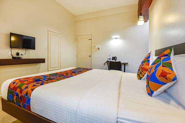 A hotel room with a bed, a television mounted on the wall, a desk with a chair, and a door.