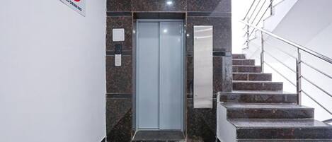 A modern elevator with a glass door, a marble wall, and a metal staircase with a handrail.