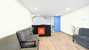 A reception area with a black desk, two grey sofas, a blue door, and a plant. - FabHotel Twamev (New Delhi)