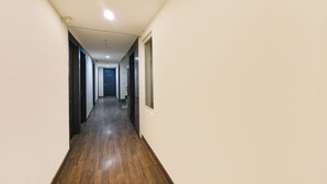 A narrow hallway with a wooden floor, a door at the end, and a window on the right wall. - FabHotel Twamev (New Delhi)