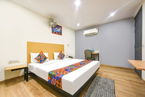 A hotel room with a bed, a desk, a chair, a fan, an air conditioner, and a door. - FabHotel Twamev (New Delhi)