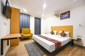A hotel room with a bed, a desk, a chair, a TV, and a painting on the wall. - FabHotel Twamev (New Delhi)