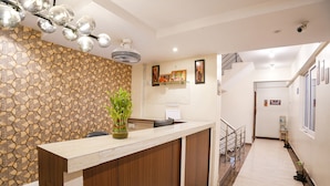 Un área de recepción con pared de diseño en piedra, un mostrador de madera, una planta en maceta y cuadros en la pared.
