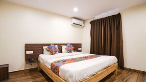 Habitación de hotel con cama de madera, pared blanca, cortina marrón y unidad de aire acondicionado.