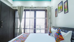A hotel room with a bed, a wardrobe, a window with curtains, and three framed pictures on the wall. - Fabhotel Keptown (Danapur)