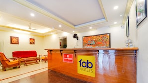 A hotel reception area with a wooden reception desk, a red sofa, and a fan. - Fabexpress Majestic Inn (Thiruvananthapuram)