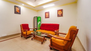 A living room with a sofa, two armchairs, a coffee table, and a ceiling fan. - Fabexpress Majestic Inn (Thiruvananthapuram)