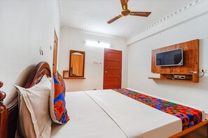 A bedroom with a bed, a ceiling fan, a TV mounted on the wall, and a door. - Fabexpress Majestic Inn (Thiruvananthapuram)