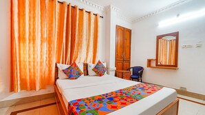 A hotel room with a bed, orange curtains, a wooden wardrobe, a chair, and a mirror on the wall. - Fabexpress Majestic Inn (Thiruvananthapuram)