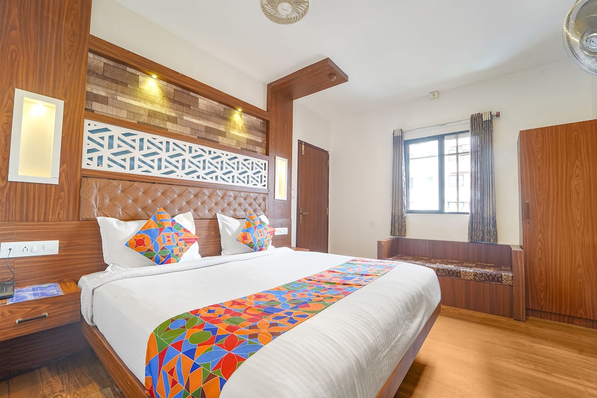 A well-lit bedroom with a large bed, a wooden headboard, a decorative wall panel, and a window with curtains.
