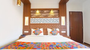 A bedroom with a wooden headboard, two bedside lamps, a patterned wall decoration, and a door. - Fabhotel Qube (Kanayannur)
