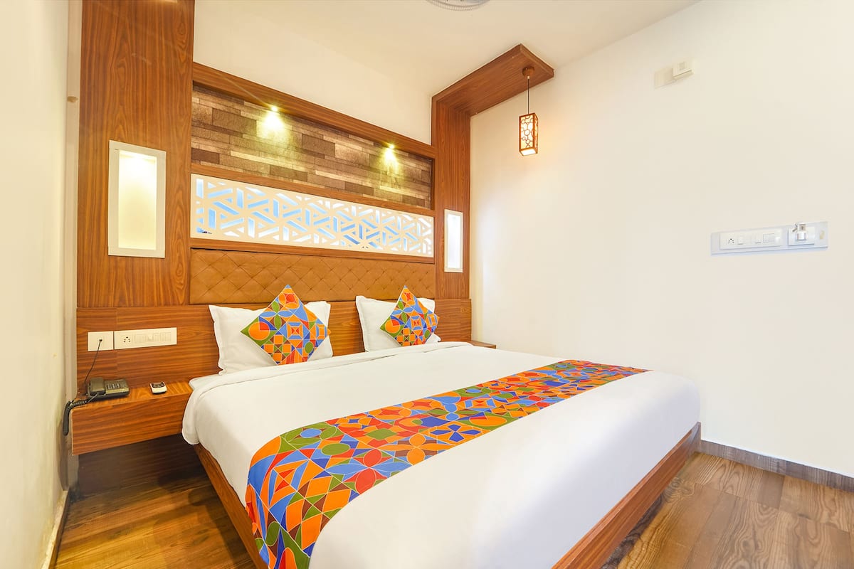 A hotel room with a wooden headboard, a patterned wall, a bed with white linens, and a colorful bedspread.