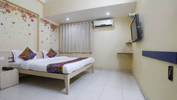 Camera d'albergo con un letto, una TV a muro, un climatizzatore e un piccolo ripiano.