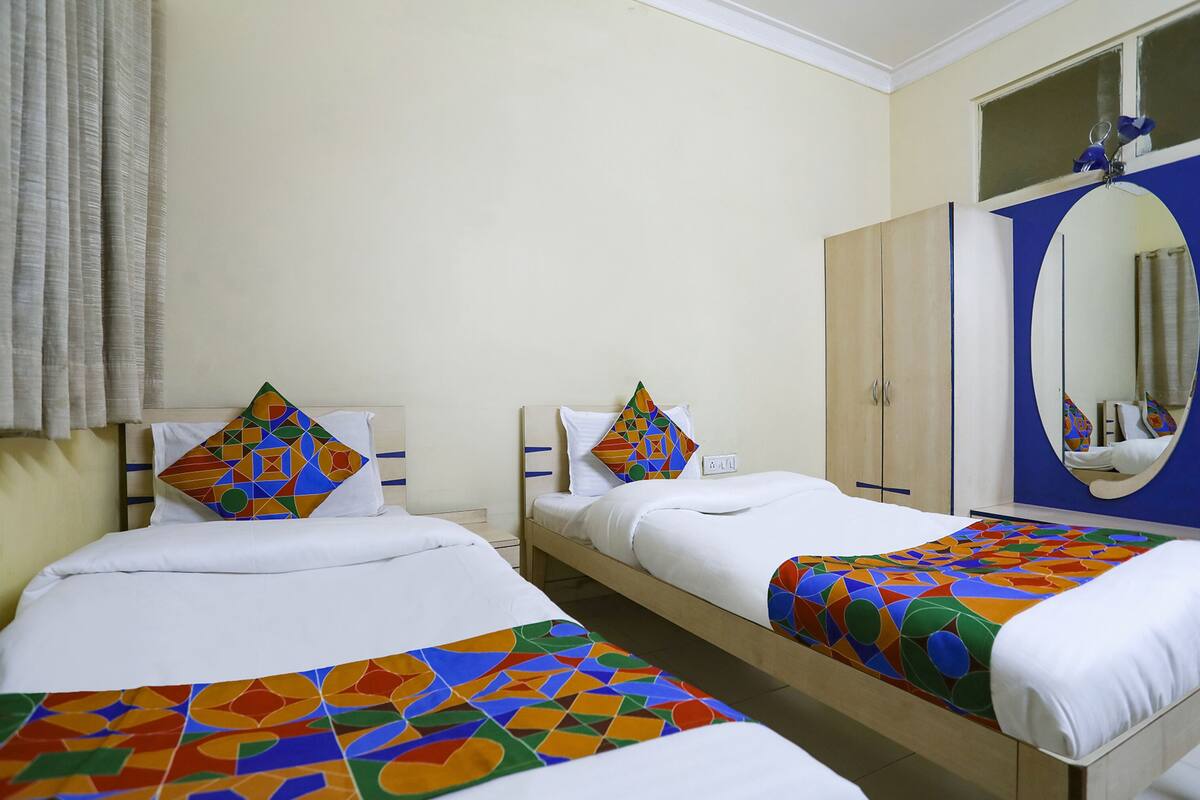 A hotel room with two single beds, each with a colorful geometric-patterned bedspread and matching pillows. There is a large mirror on the wall above the beds, and a wardrobe with a mirror door.