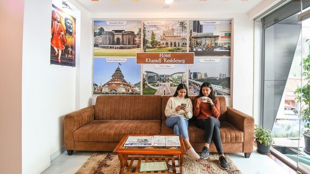 A room with a brown sofa, a coffee table with magazines, and a large poster of hotel locations. - Fabhotel Prime Kharadi Residency (Pune)