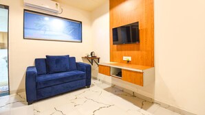 A modern room with a blue sofa, a flat-screen TV mounted on a wooden panel, and a framed picture on the wall. - Fabhotel Prime Kharadi Residency (Pune)