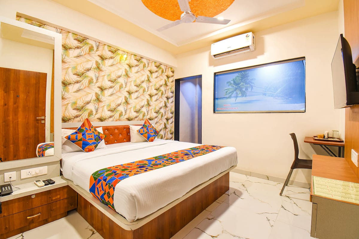 A hotel room with a bed, a desk, a chair, a mirror, and a wall-mounted TV.