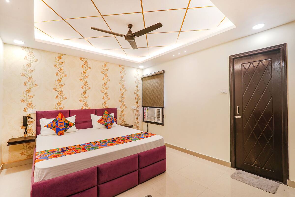 A bedroom with a bed, a ceiling fan, a wall-mounted air conditioner, and a door.