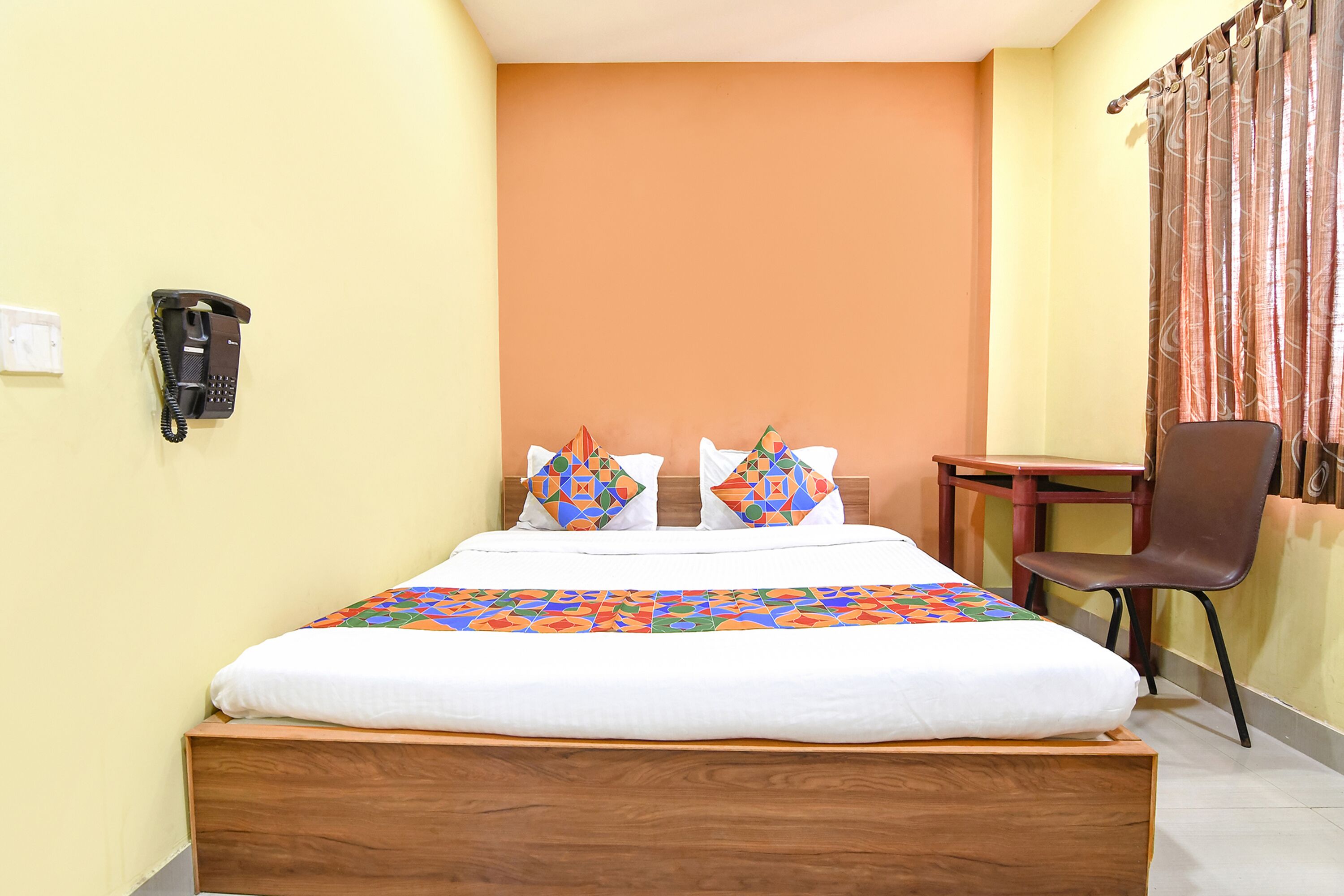 A hotel room with a wooden bed, a desk, a chair, and a telephone on the wall.