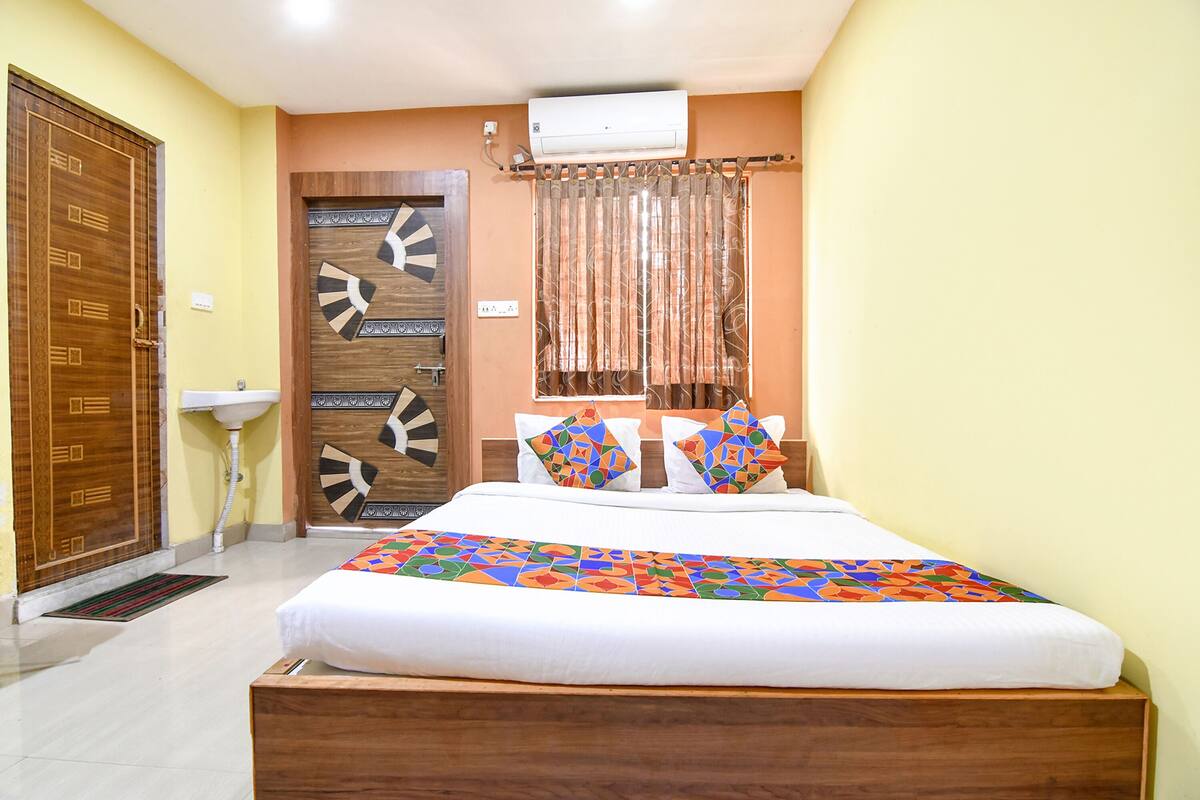 A bedroom with a wooden bed, a white bedside table, a wooden wardrobe, a ceiling fan, and a window with curtains.