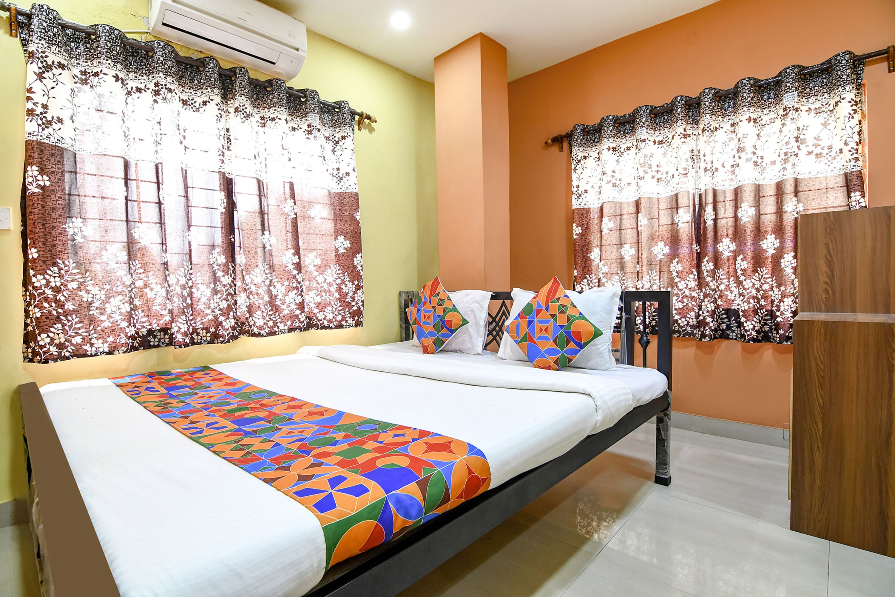 A neatly made bed with a colorful geometric-patterned bedspread, a wooden headboard, and decorative pillows.