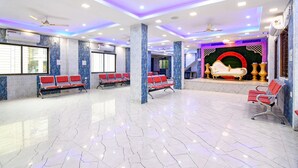 A spacious lobby with a marble floor, red seating, and a stage with a red circular design. - Fabhotel Santoshi (Kolkata)