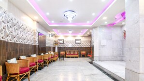 A reception area with a long row of wicker chairs with red cushions, a reception desk, and a decorative wall with a geometric pattern. - Fabhotel Santoshi (Kolkata)