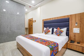 A hotel room with a large bed, a wooden headboard, a colorful bedspread, a bedside table with a phone, and a marble wall. - Fabhotel National (Mumbai)