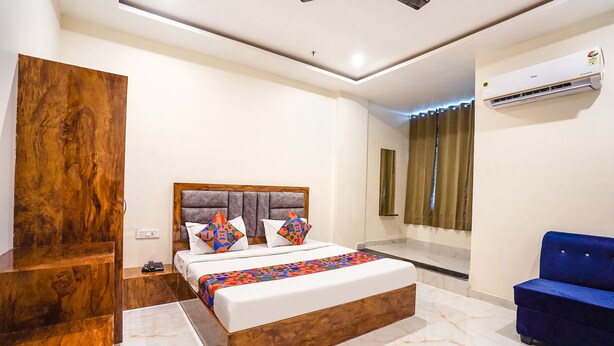 A modern bedroom with a wooden headboard, a large bed with colorful bedding, a blue sofa, and an air conditioning unit on the wall. - Fabhotel Kyshna Inn (Mathura)