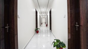 A long, narrow hallway with white walls and a shiny floor, flanked by wooden doors on both sides. - Fabhotel Kyshna Inn (Mathura)