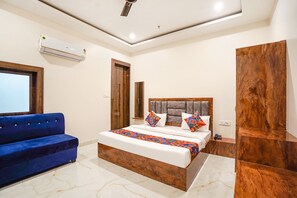 A modern bedroom with a large bed, a blue sofa, and a wooden wardrobe. - Fabhotel Kyshna Inn (Mathura)