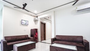 A modern living room with two sofas, a coffee table, a ceiling fan, and a mounted TV. - Fabhotel Kyshna Inn (Mathura)