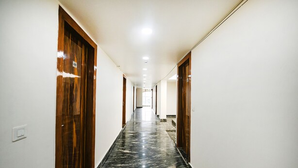 Un pasillo largo y estrecho con puertas de madera a ambos lados y piso de mármol negro.
