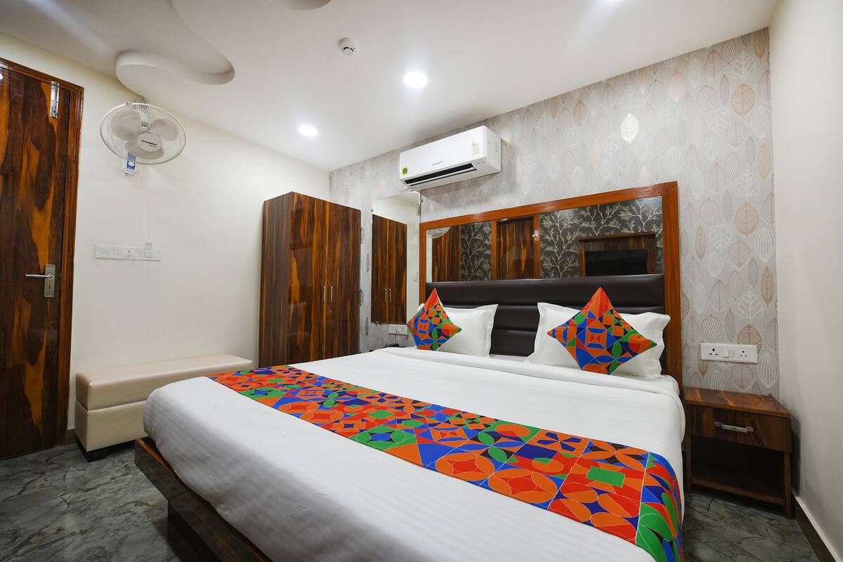 Une chambre d’hôtel avec un lit, une armoire en bois, une petite table de chevet et un appareil de climatisation fixé au mur.