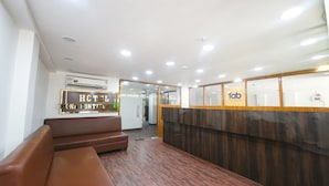 Zona de recepción de un hotel con un mostrador de madera, un banco de cuero marrón y una unidad de aire acondicionado en la pared.