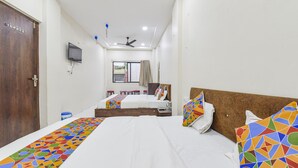 A hotel room with two beds, a television, a ceiling fan, and a window with curtains. - Fabexpress Devani Palace (Ujjain)