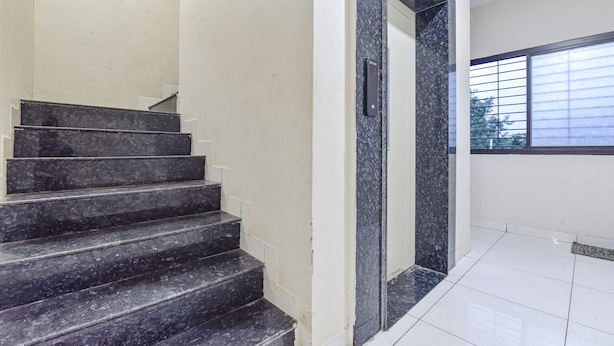 A set of black marble stairs leading to a doorway with a glass panel, white walls, and a window with blinds. - Fabexpress Devani Palace (Ujjain)