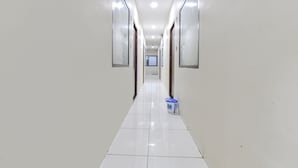 A long, narrow hallway with white walls and a shiny tiled floor. - Fabexpress Devani Palace (Ujjain)