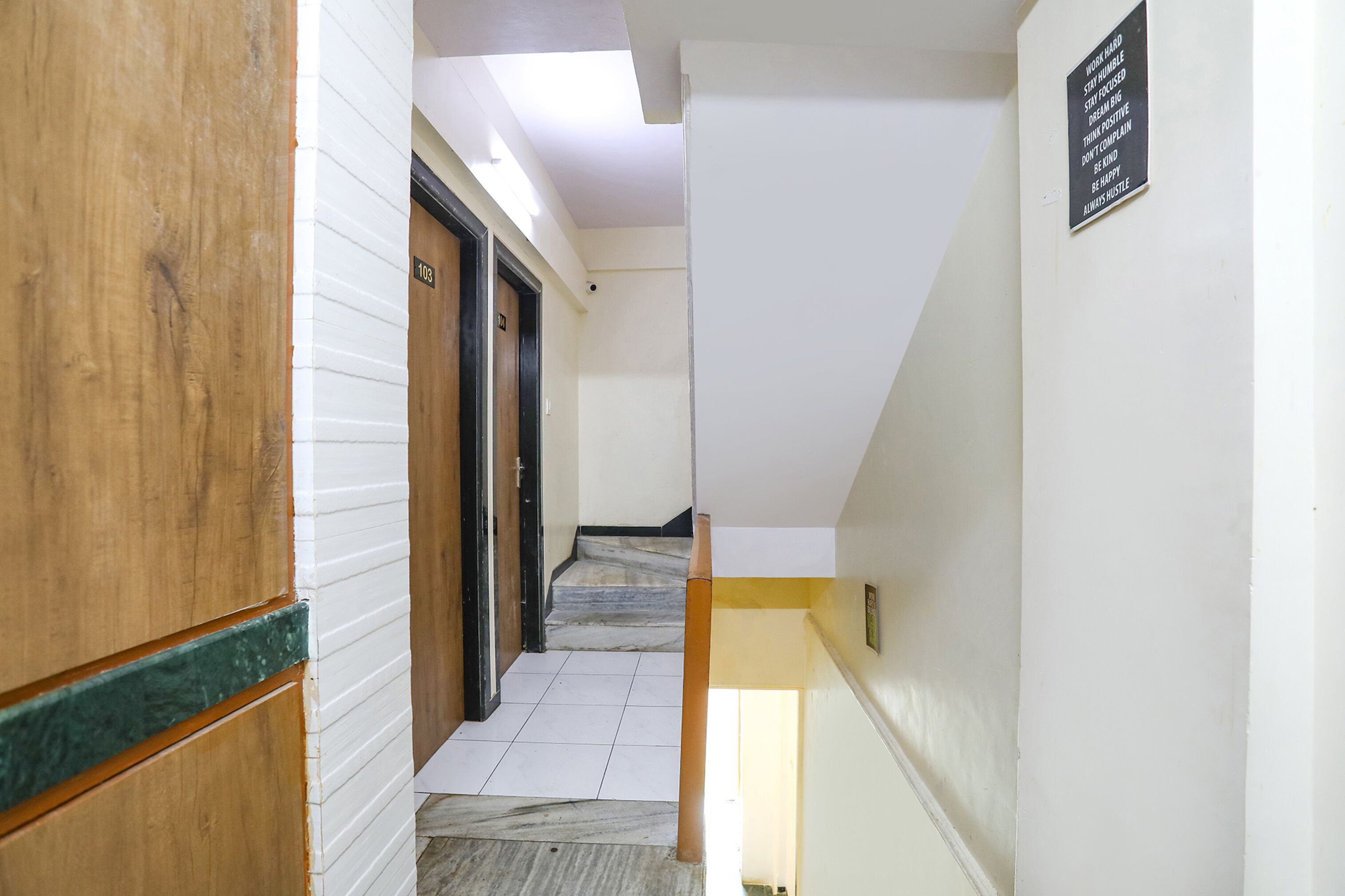 A hallway with a wooden door, a marble staircase, and a sign on the wall.